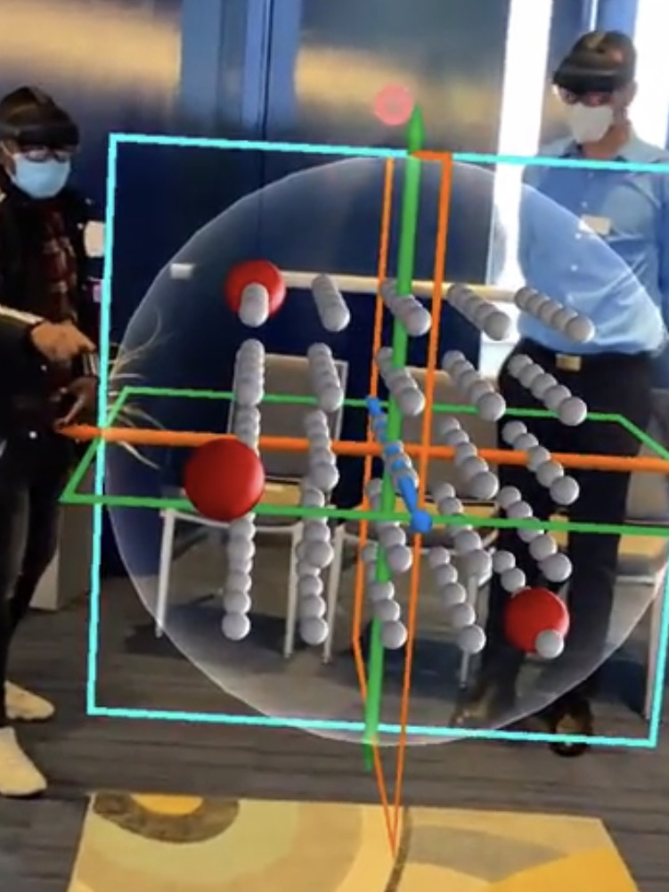 A teacher wearing a VR headset gestures with her hands to manipulate a life-sized hologram of a neurotransmitter receptor