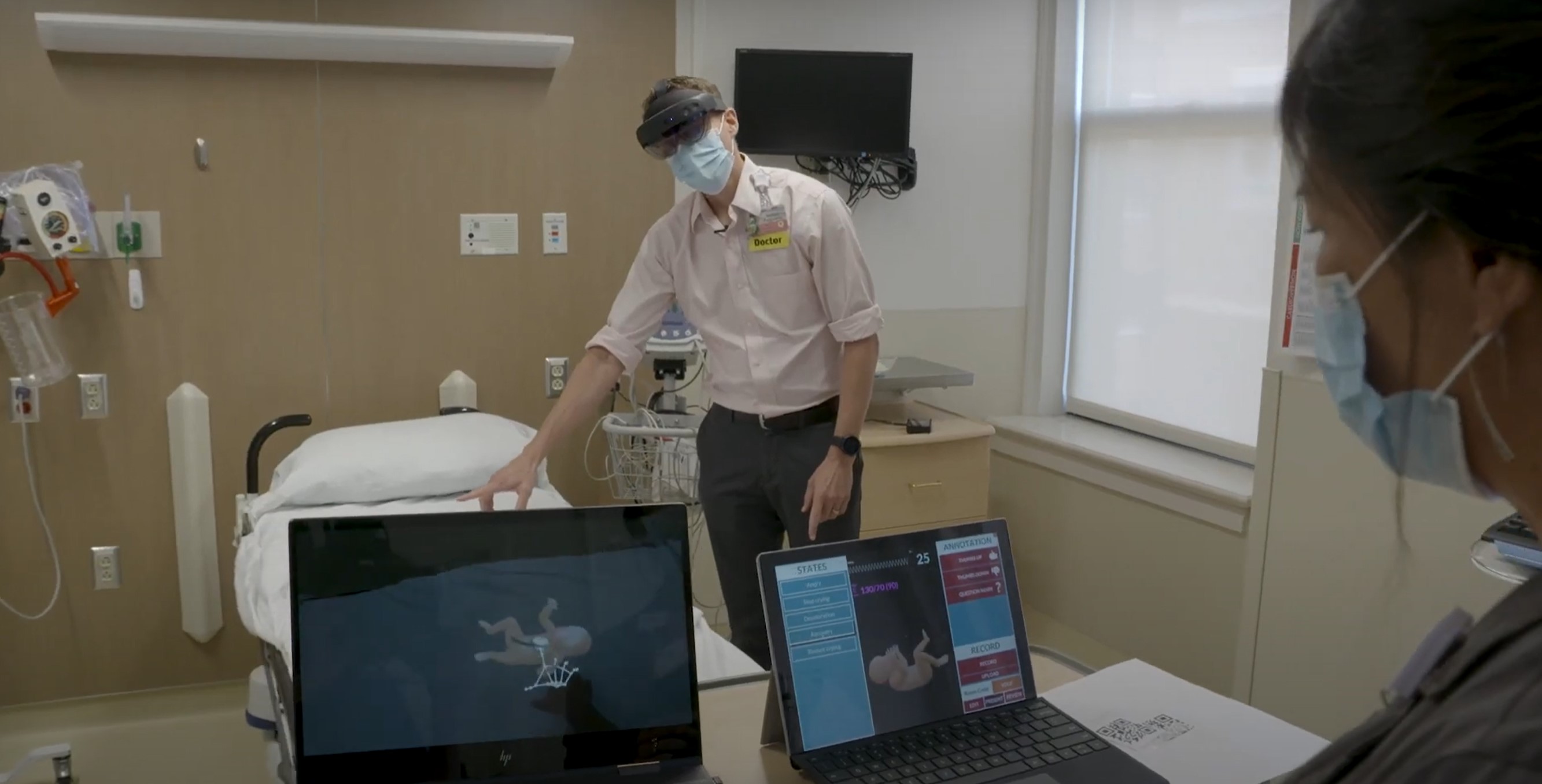 A portable simulation kit open on a table in a rural hospital setting. A holographic baby overlay is visible on a small mannequin, with clinical staff gathered around.