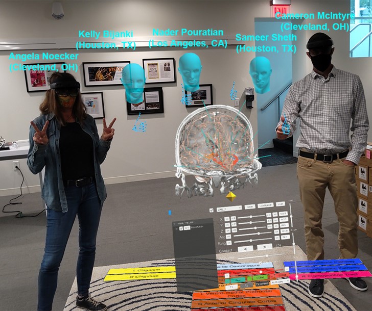 Two surgeons in different locations viewing the same holographic brain model, with one pointing to a neural pathway while the other observes in real-time.